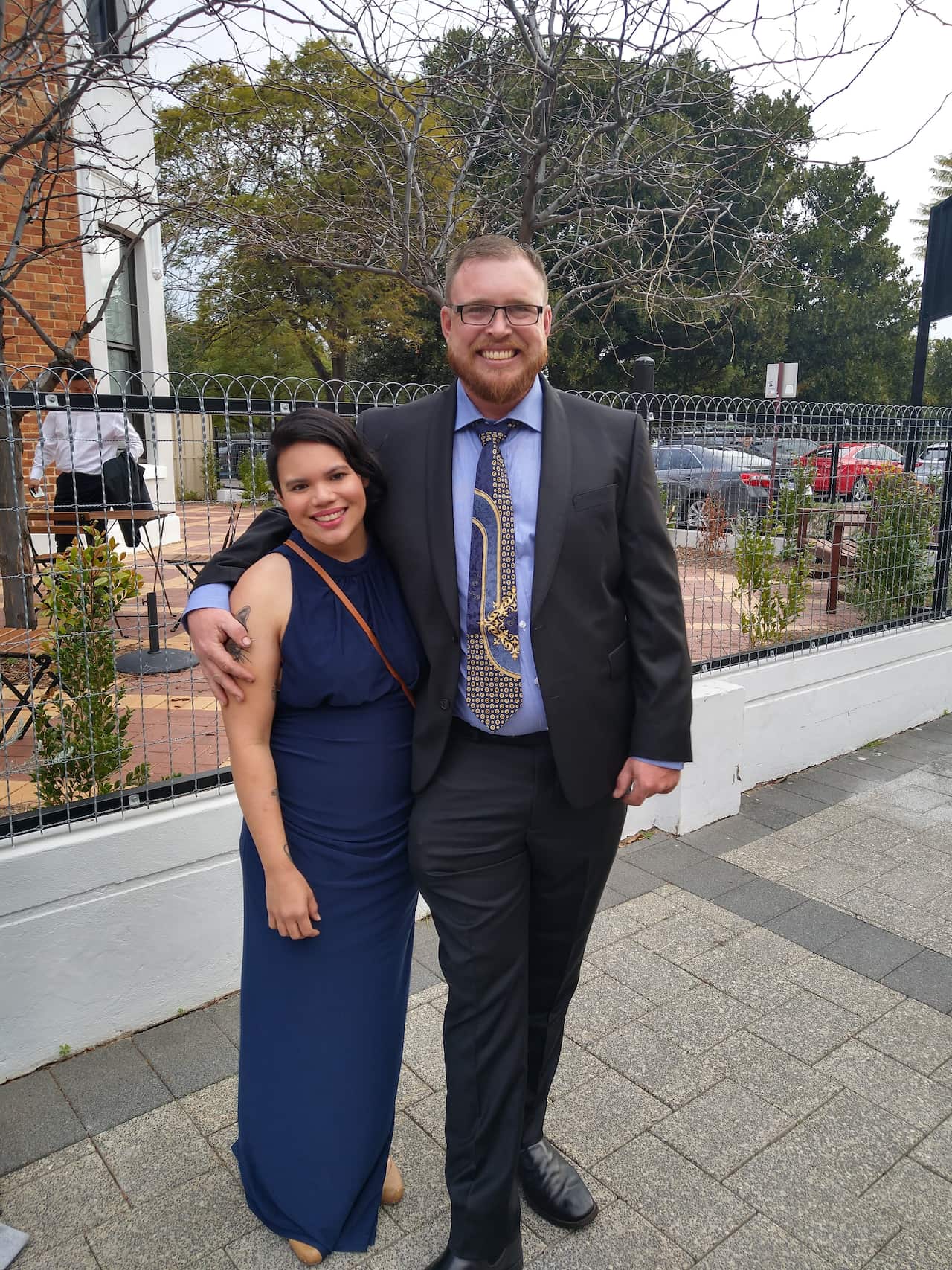 A man and a woman embrace as they smile at the camera.