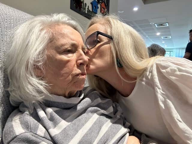 a middle aged blonde woman kissing her elderly mum's cheek in the hospital