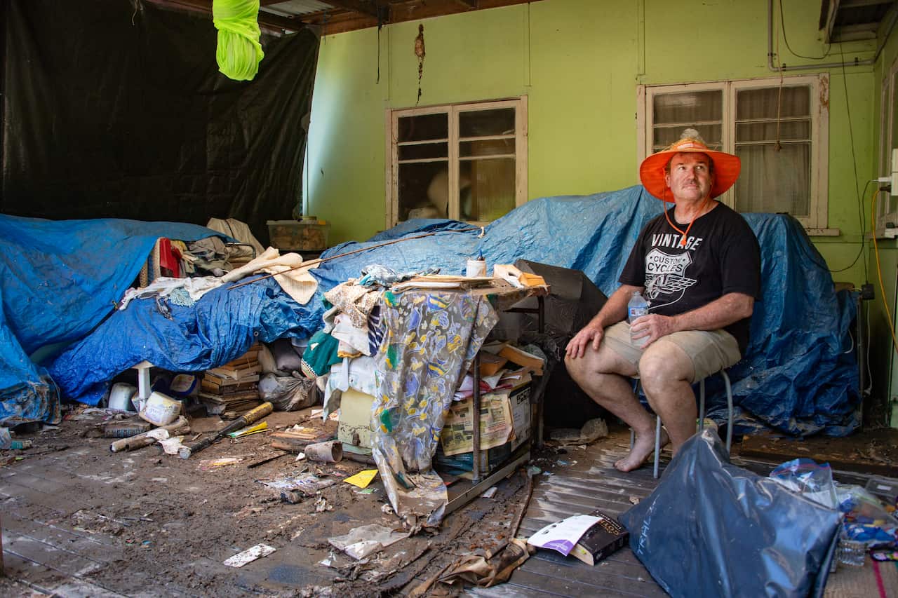 A man sits among damaged machinery after a flood.