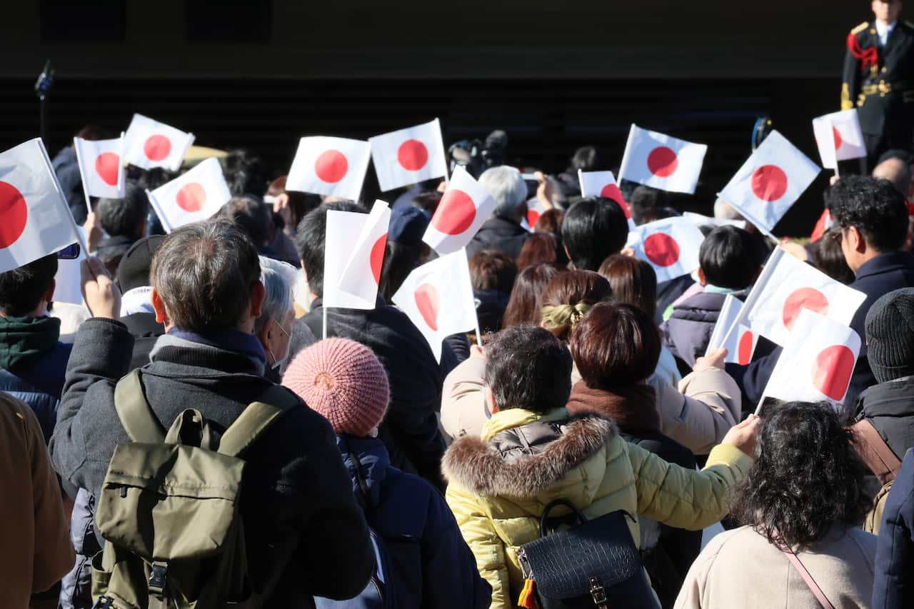 A crowd of people waves mini japanese flags above their heads