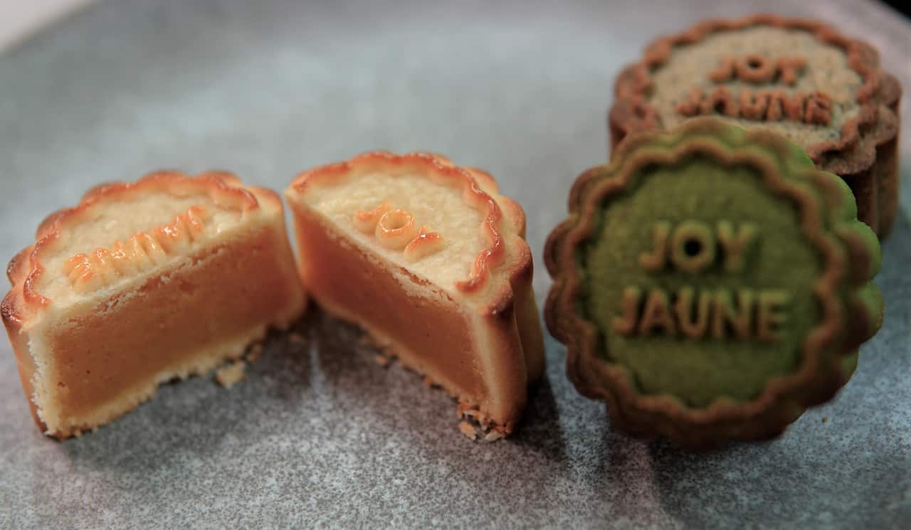 Three colourful mooncakes on a table. One is cut open to show a soft centre. The cakes have the words Joy Jaune written on them.
