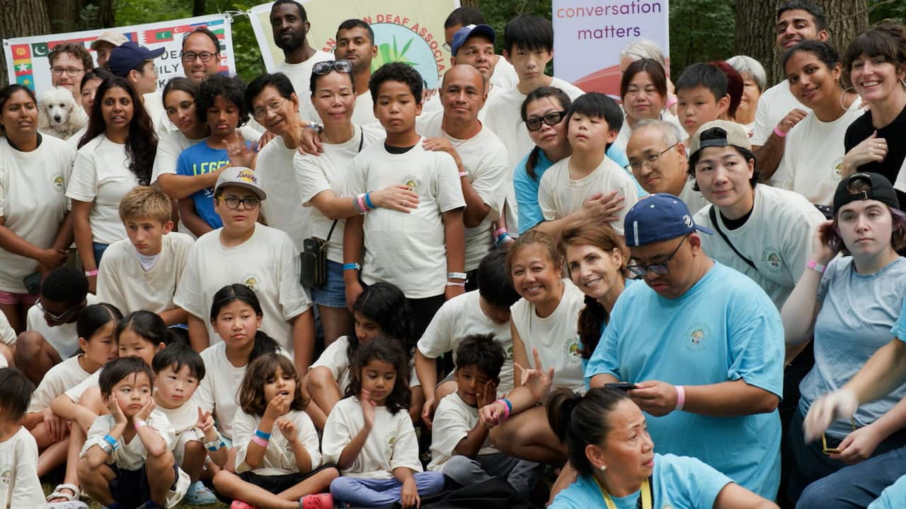 A group of children and adults wearing white or blue t-shirts are posing for a group photo 