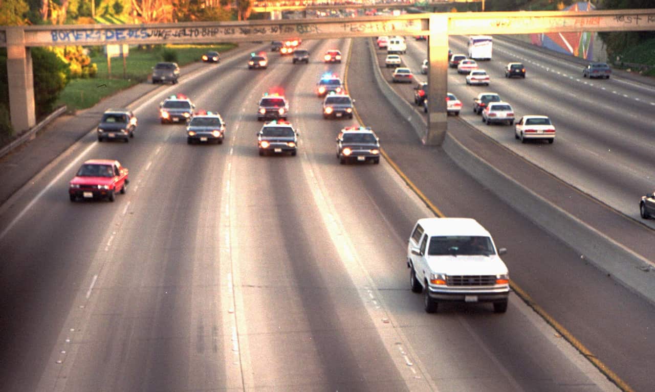 A white car is being pursued on a freeway by several police cars.
