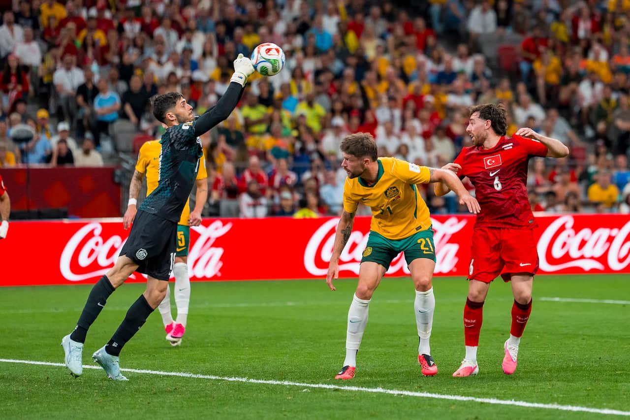 A goalkeeper wearing an all black kit leaps to punch the ball away.