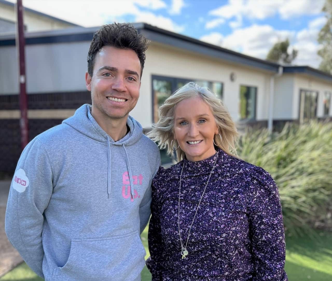 A man in a grey hoodie stands next to a woman in a purple floral short.