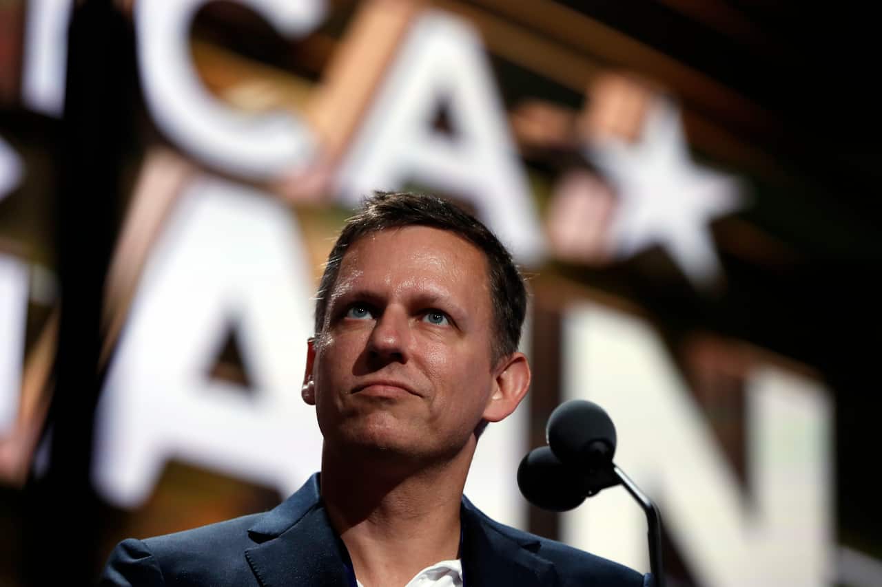 A man stands in front of a microphone, looking to his left. He has a neutral facial expression.