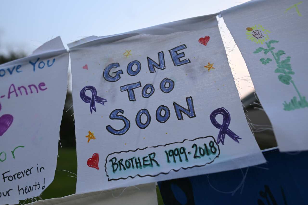 A few white posters are hanging on the street. One of them says "Gone too soon, brother - 1999 to 2018."