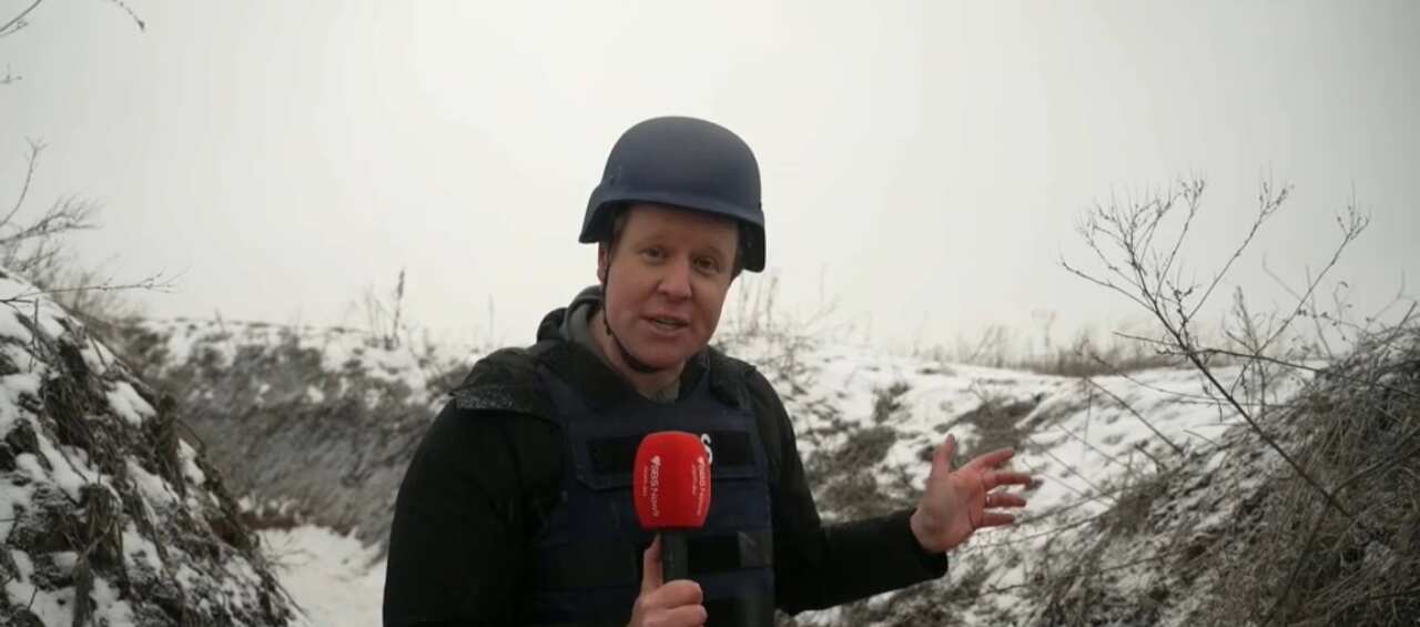 Reporter stands with red microphone and a helmet in the snow. 