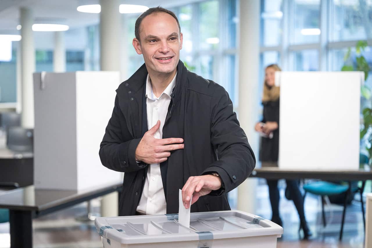 A man in a black jacket puts a ballot in a box