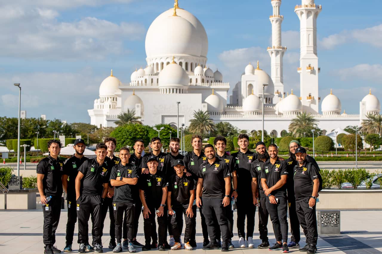 A group of young men smile at the camera standing in front of Sheikh Zayed Grand Mosque in Abu Dhabi.