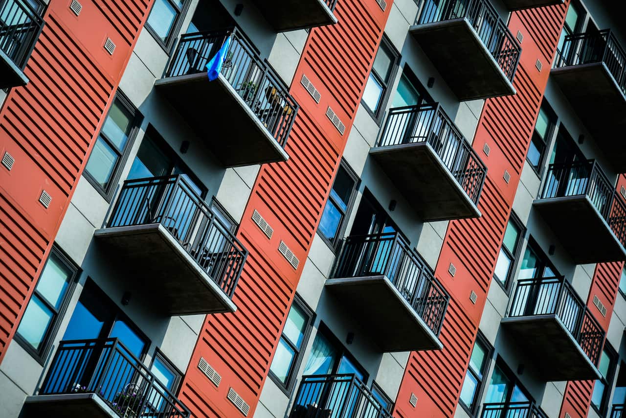 The exterior of an apartment building viewed at an angle, with rows of identical balconies and orange-and-grey walls