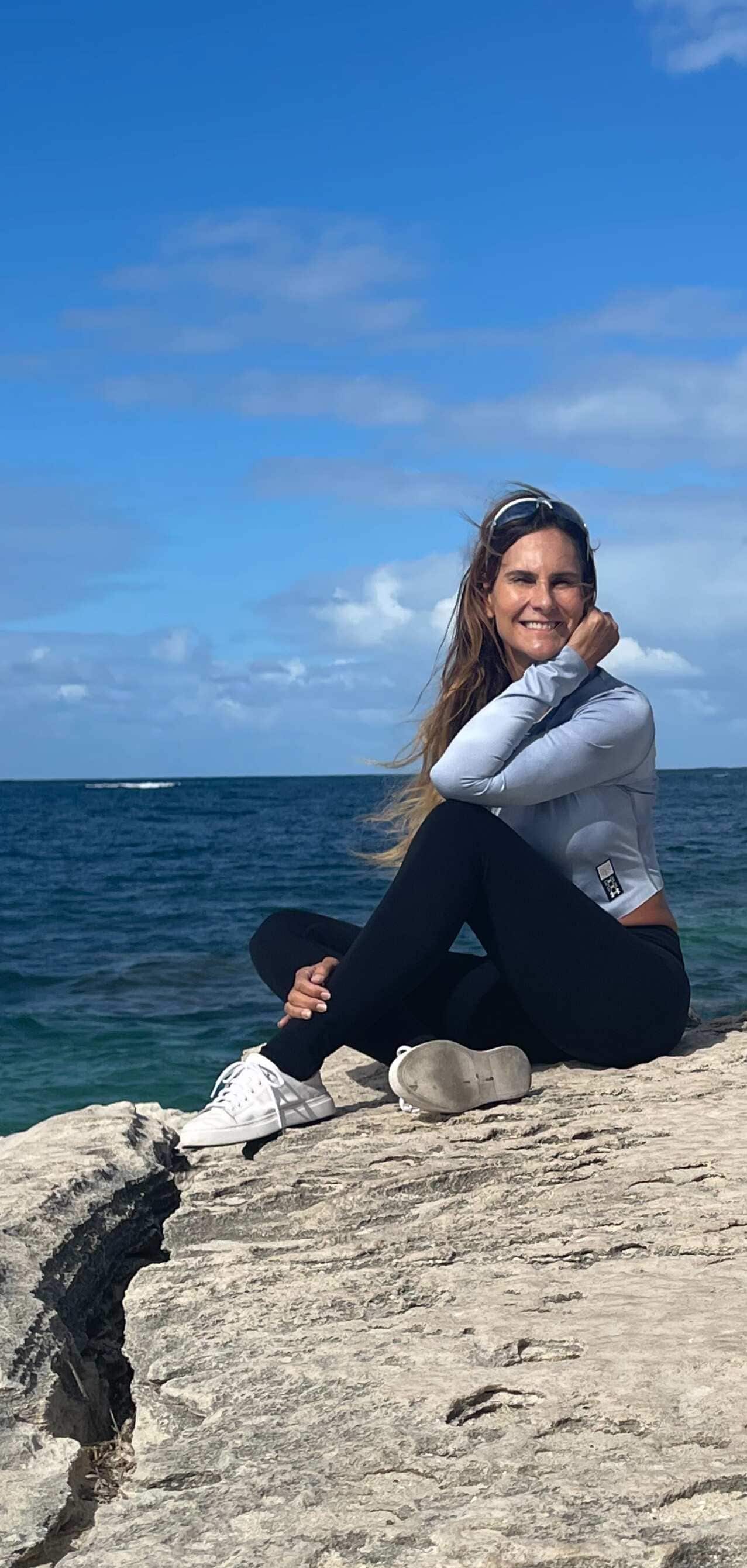 A woman in activewear sits on the rocks by the sea.