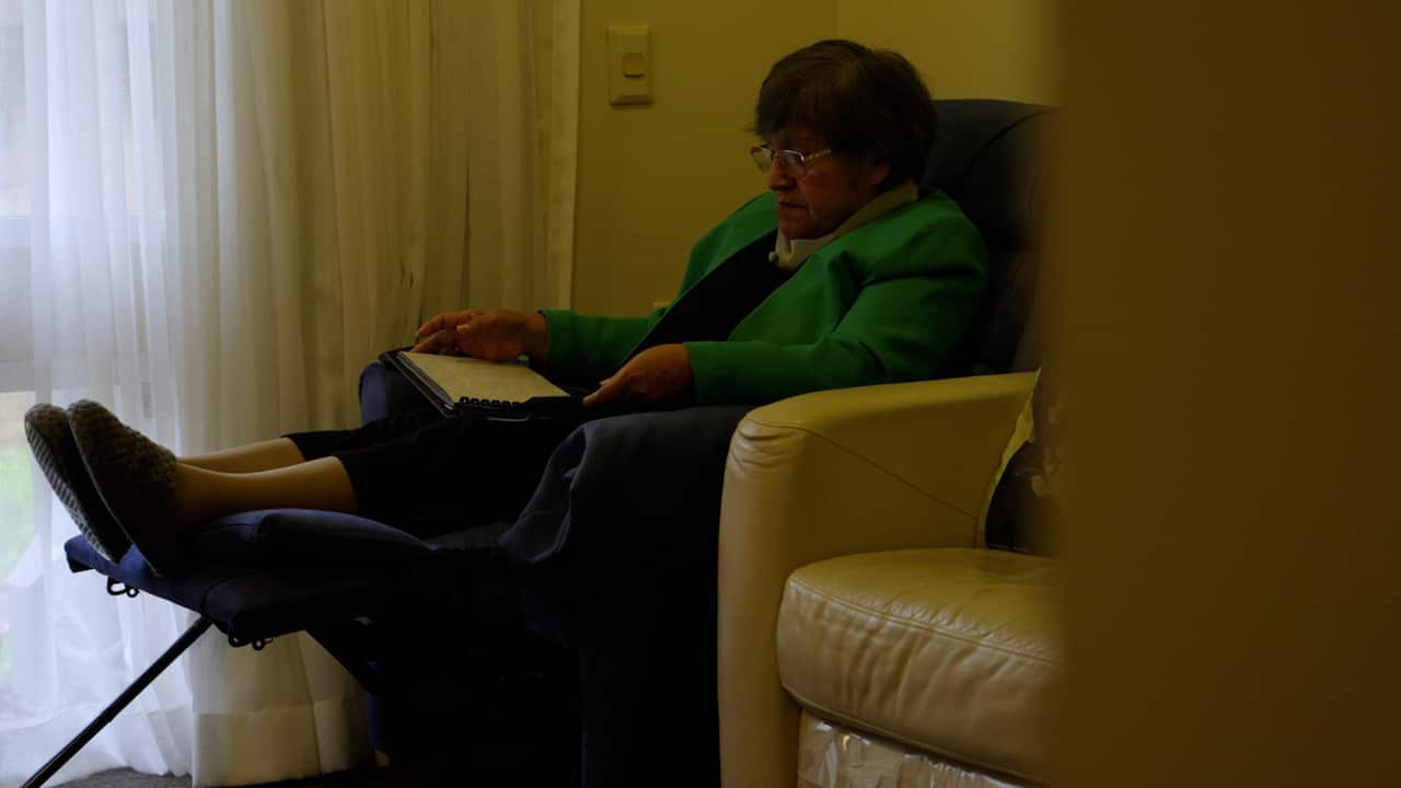 Graciela at home reading a book and sitting in a chair.
