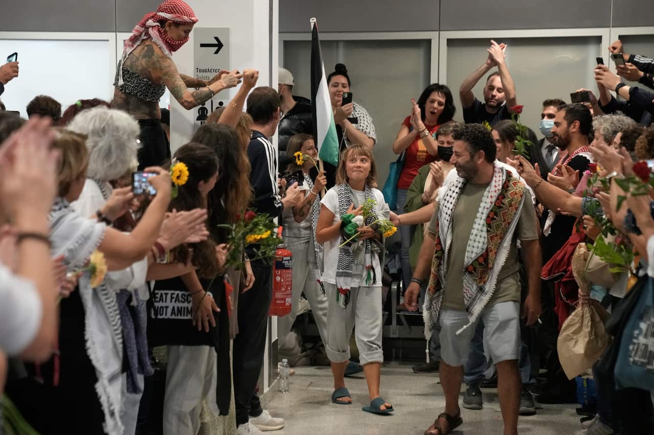 A young woman walks into an airport terminal surrounded by crowds of supporters.