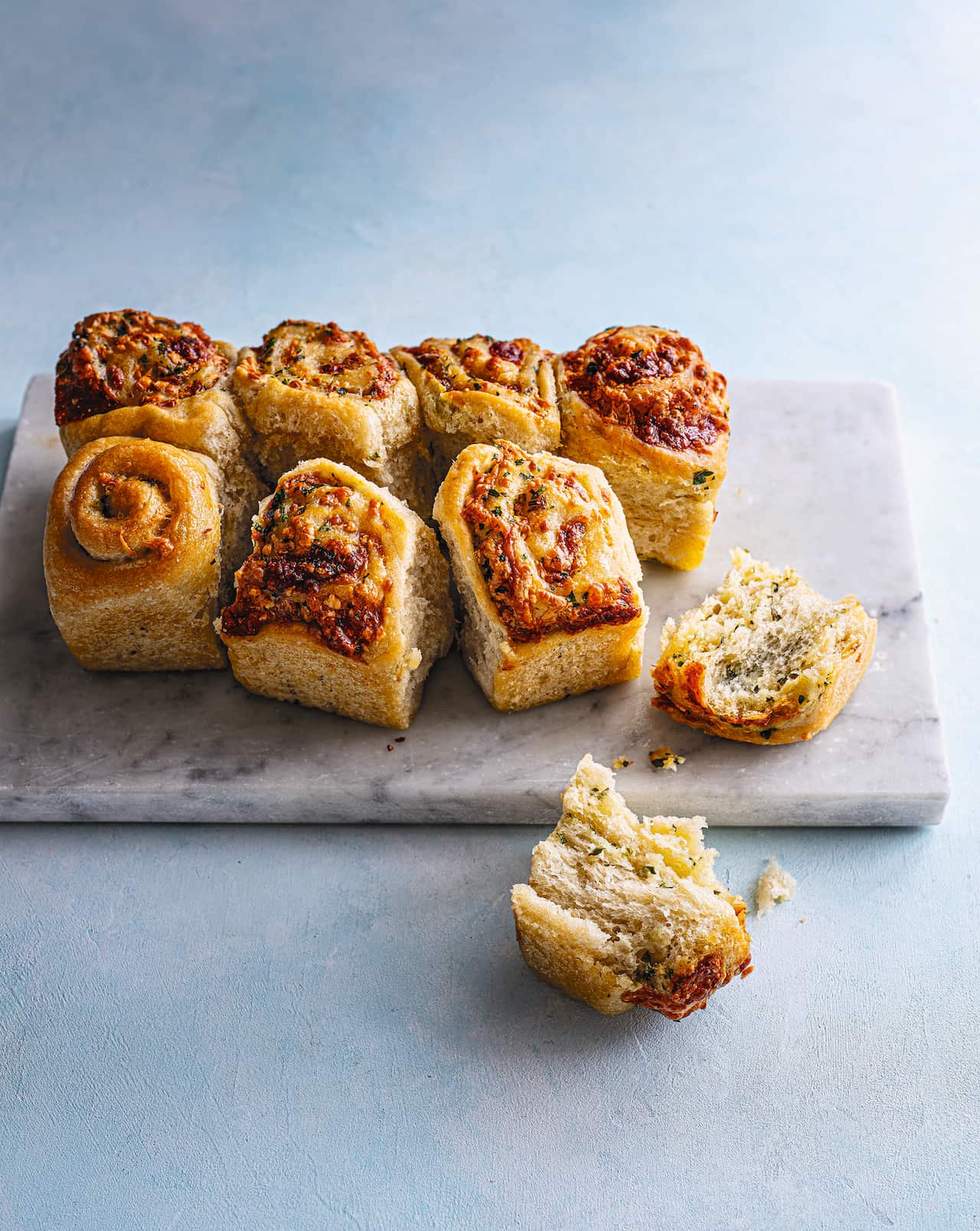 Seven bread scrolls sit on a board. Another, torn in two, lies alongside. 