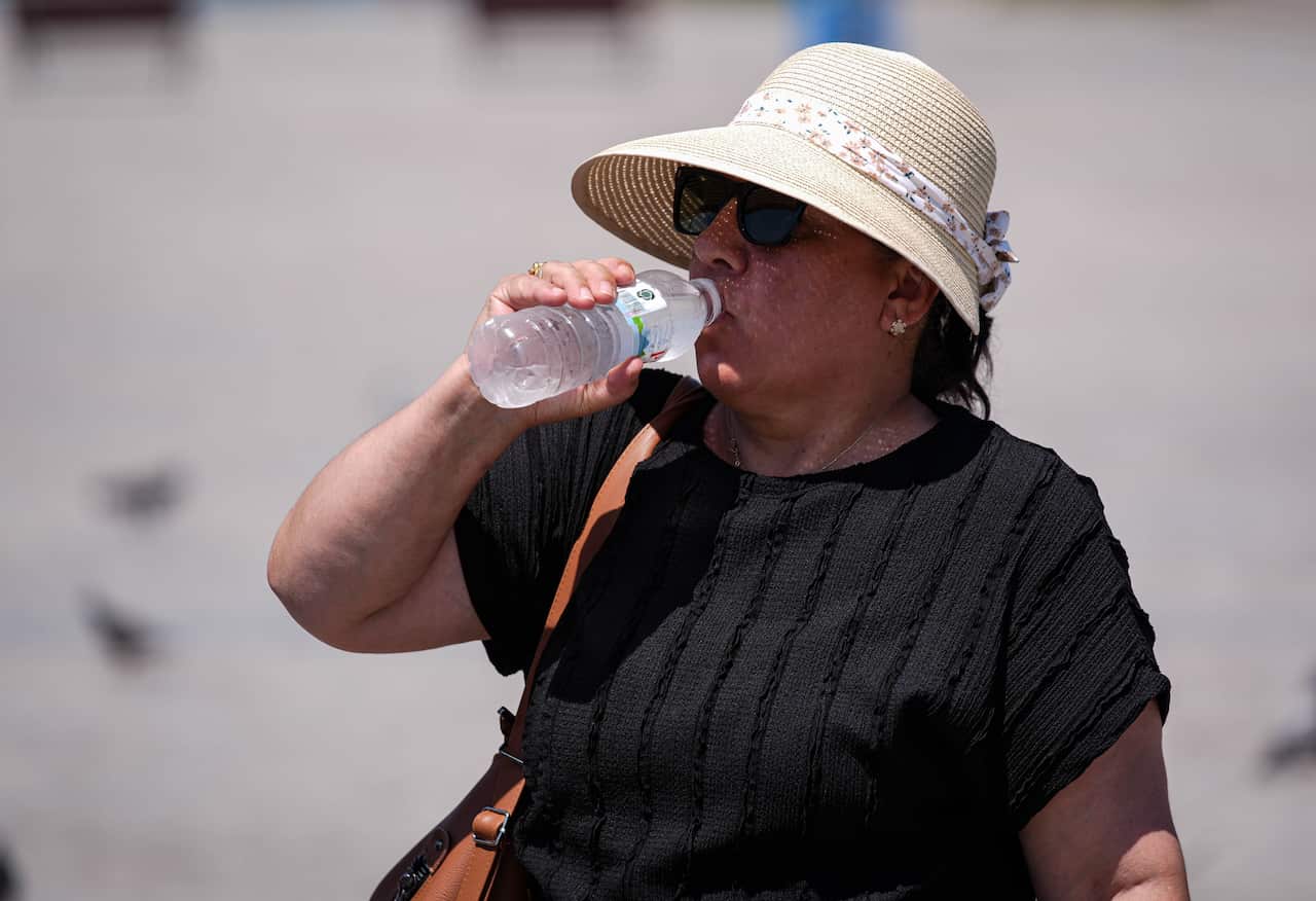 A woman wearing a white hat outside drinking from a clear plastic water bottle