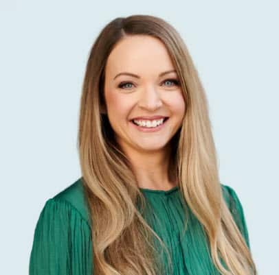 A woman with long brown hair and a green shirt smiles at cmera.