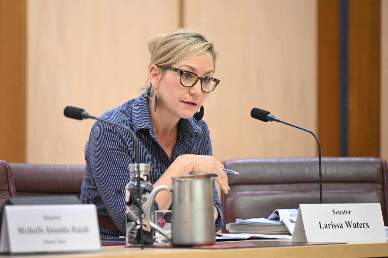 A woman with blonde hair and dark-framed glasses and wearing a blue shirt sits at a table
