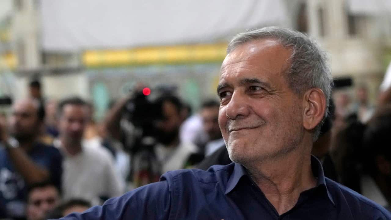 Masoud Pezashkian staring left and smiling. There is a crowd of people behind him.