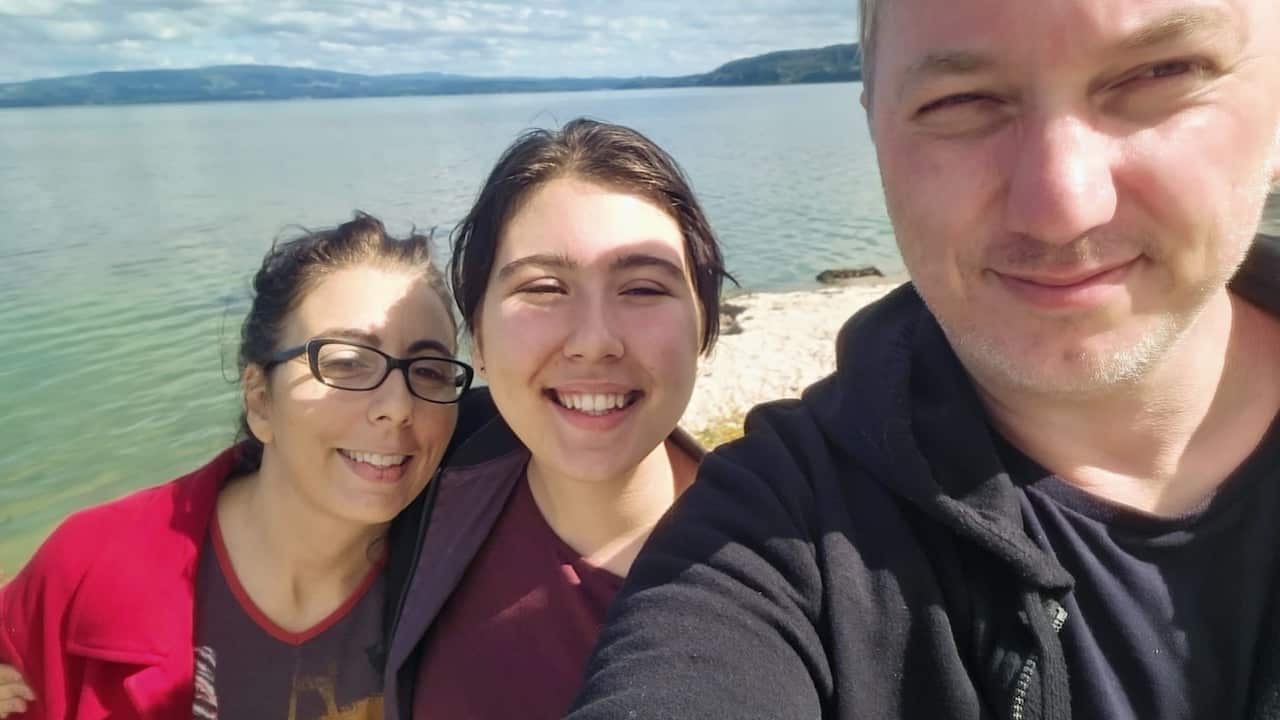 a middle aged woman, young woman and middle aged man smile into a camera taking a selfie in front of a lake