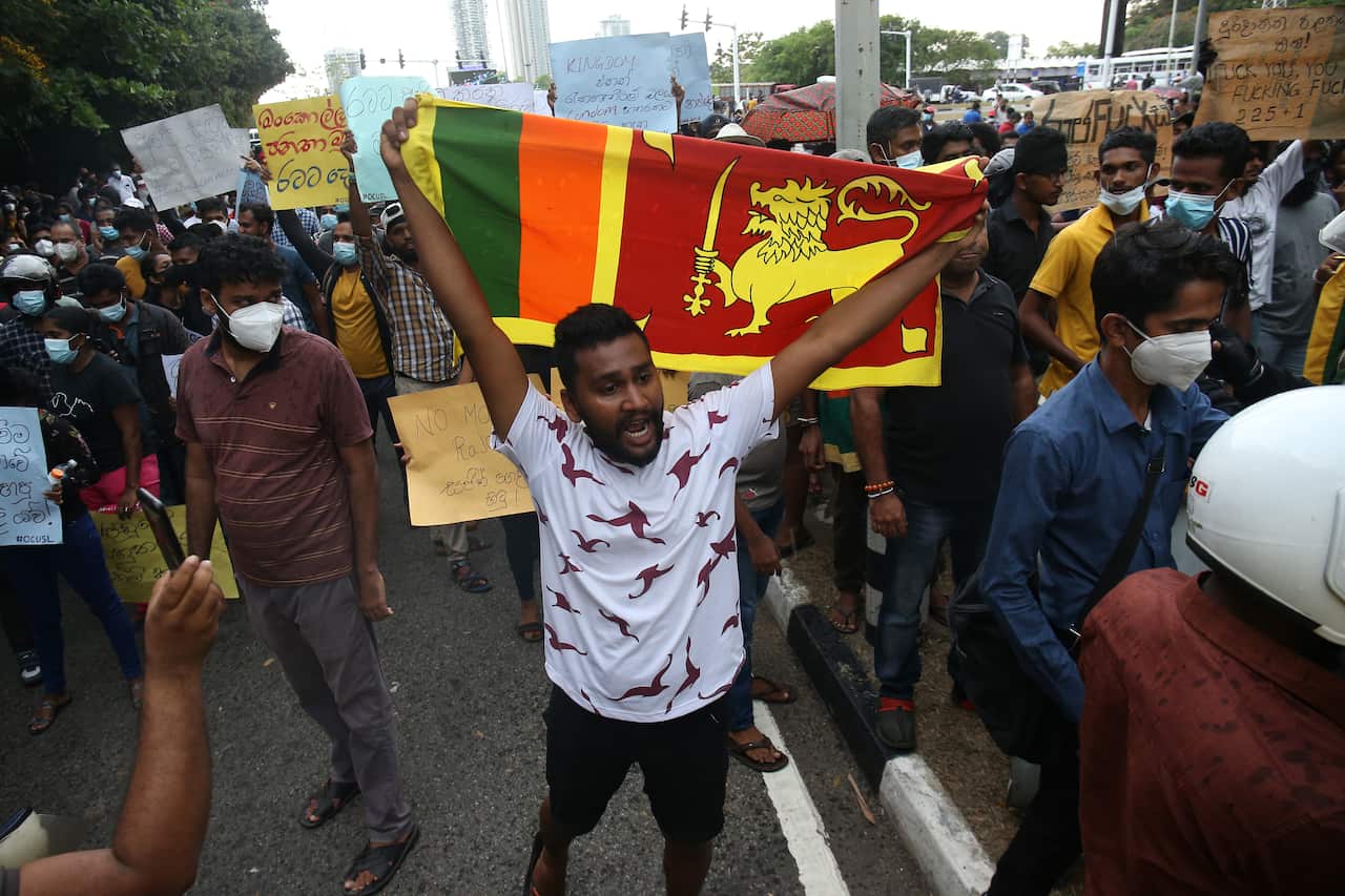 A demonstrator is seen standing amid a crowd of protesters holding the flag of Sri Lanka above his head.