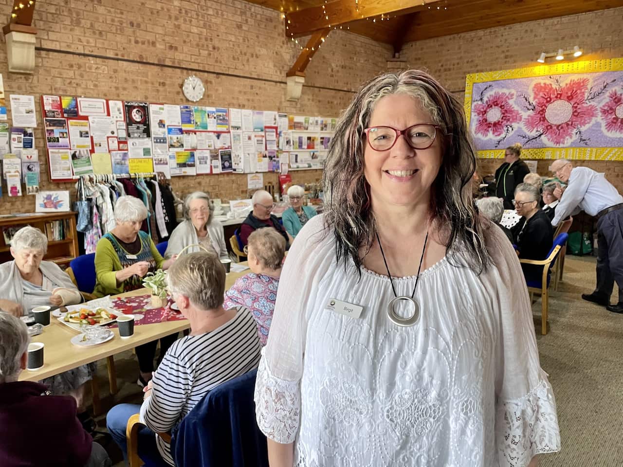 A woman stands in front of a table with people sitting at it.