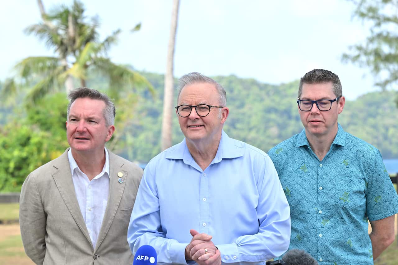 Three men standing next to each other. There are trees in the background.