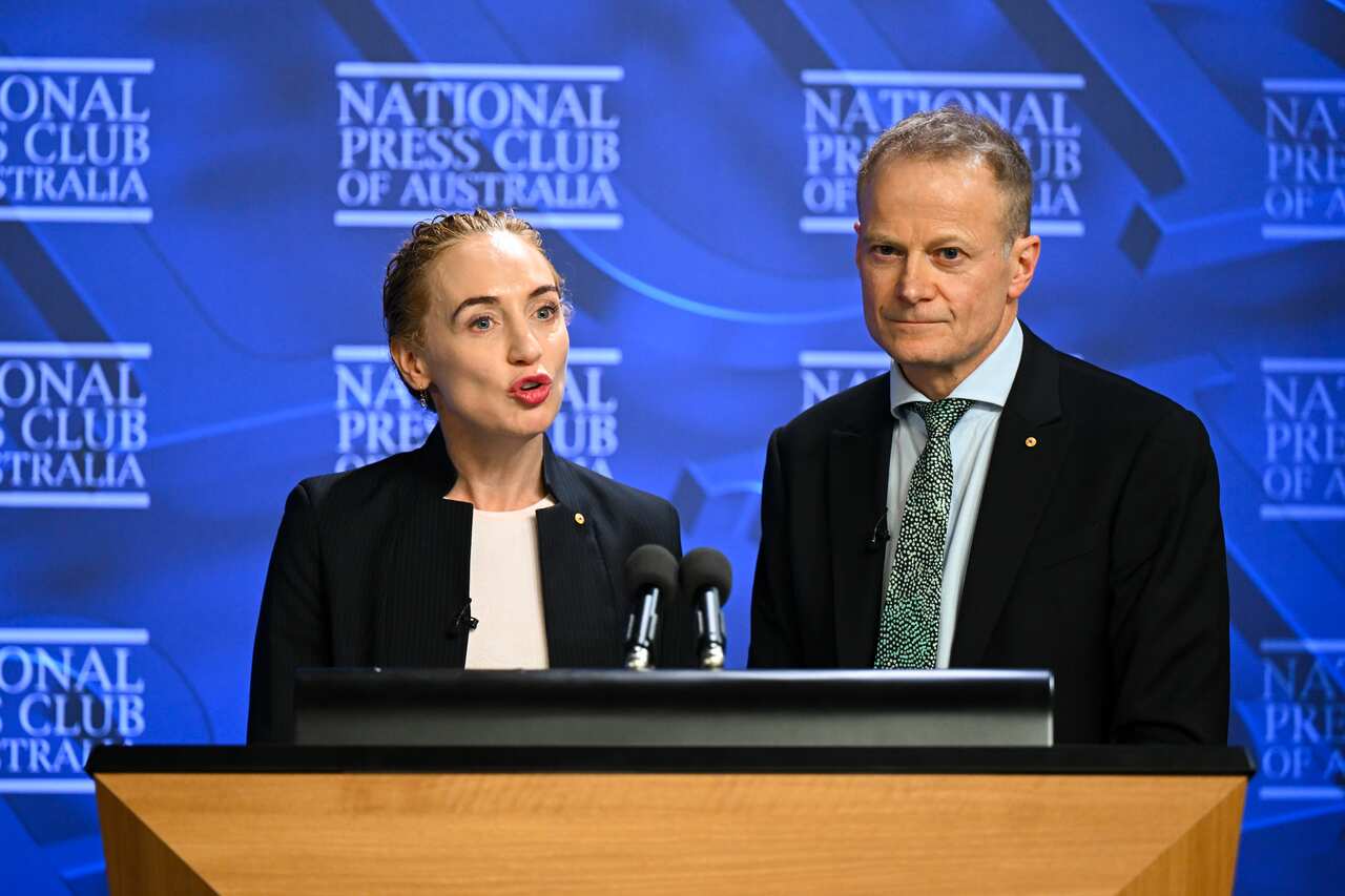 A woman and man deliver a speech from a lectern