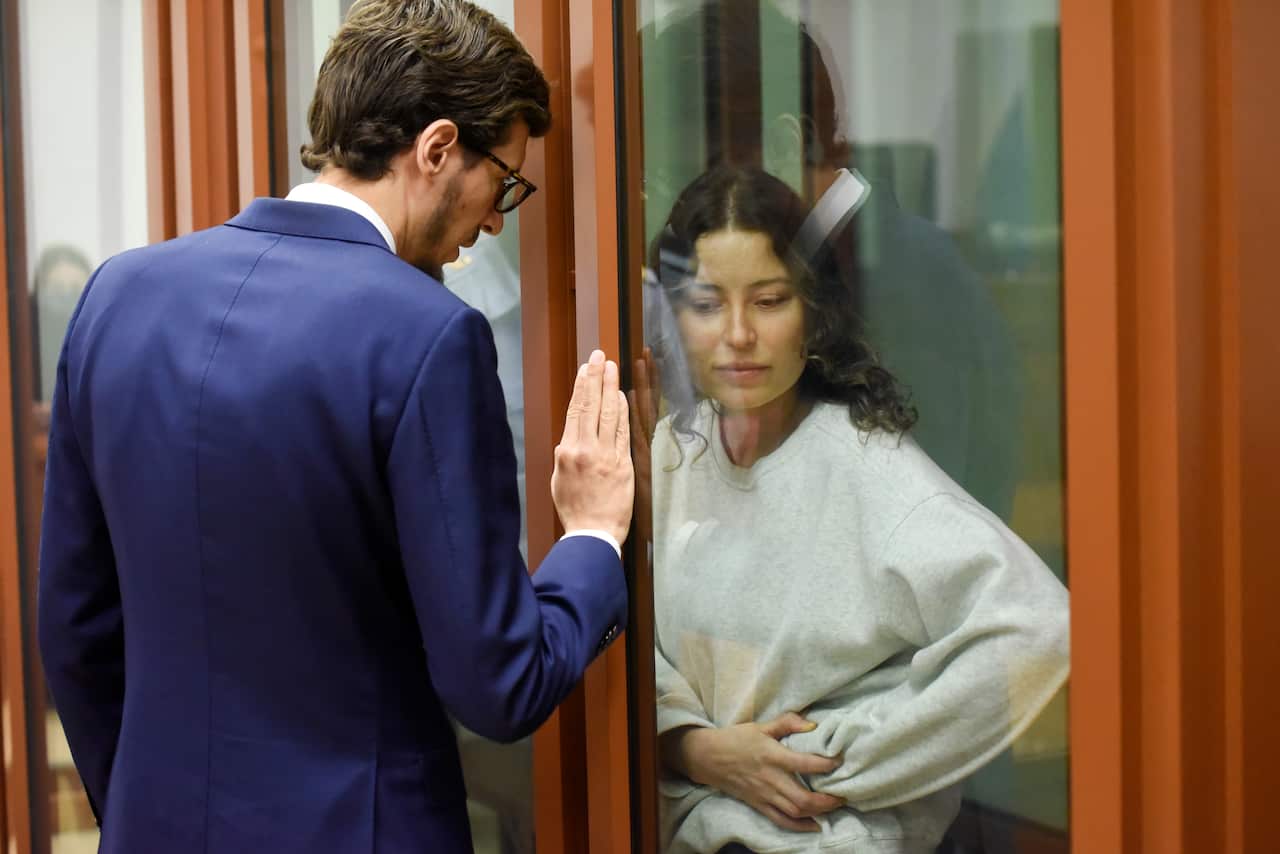 A male lawyer in a blue suit standing on other side of a glass cage where a female prisoner is being held