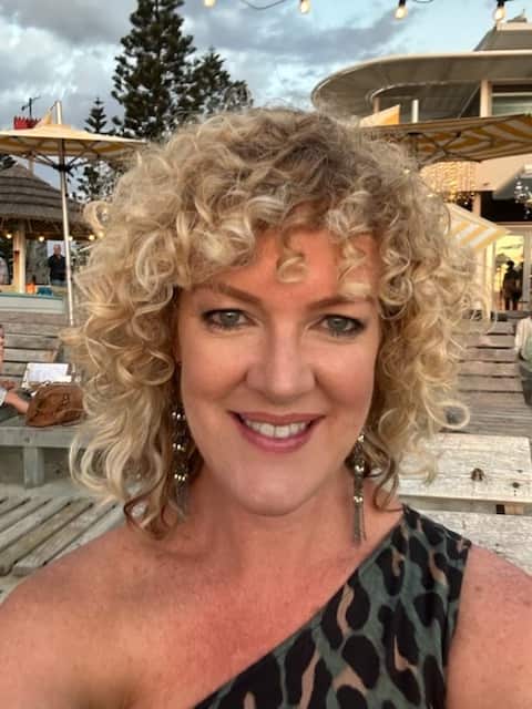 A portrait shot of a middle aged woman with shoulder-length curly hair smiling at the camera.
