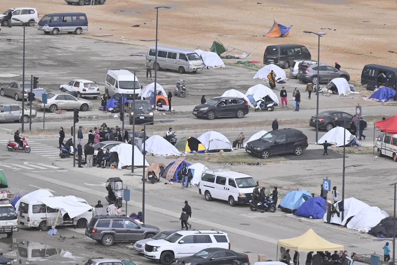 People standing near cars and tents along an intersection.
