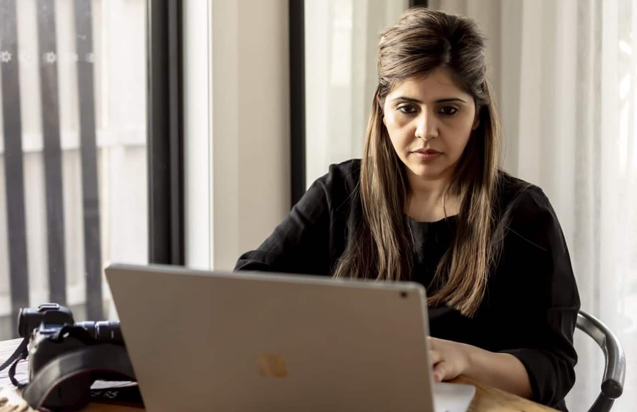 A woman wearing a black top works at her laptop, her face set in a serious expression.