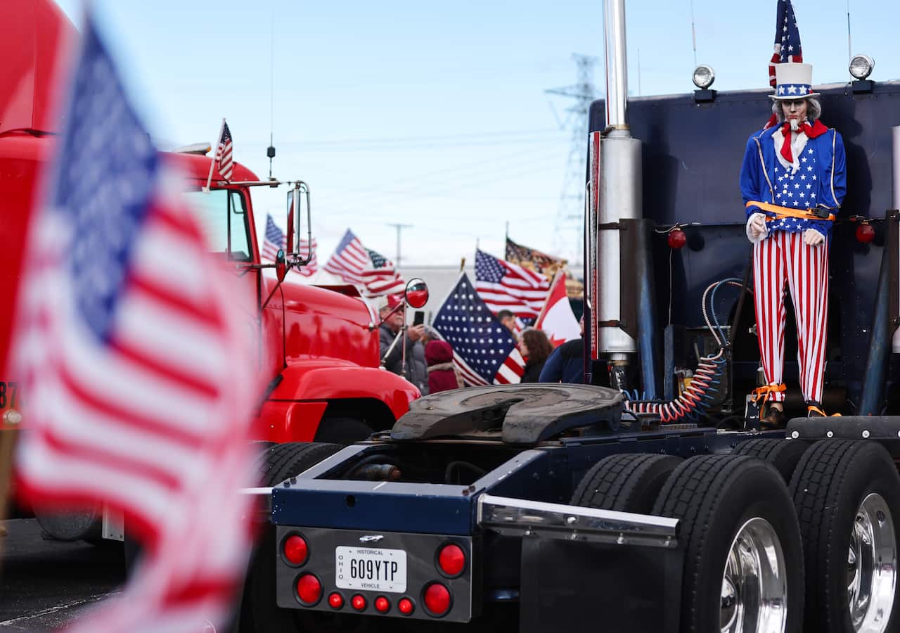 Two trucks are seen with people holding United States flags in the background.