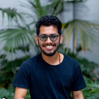 A man wearing glasses and a t-shirt in front of a large fern.
