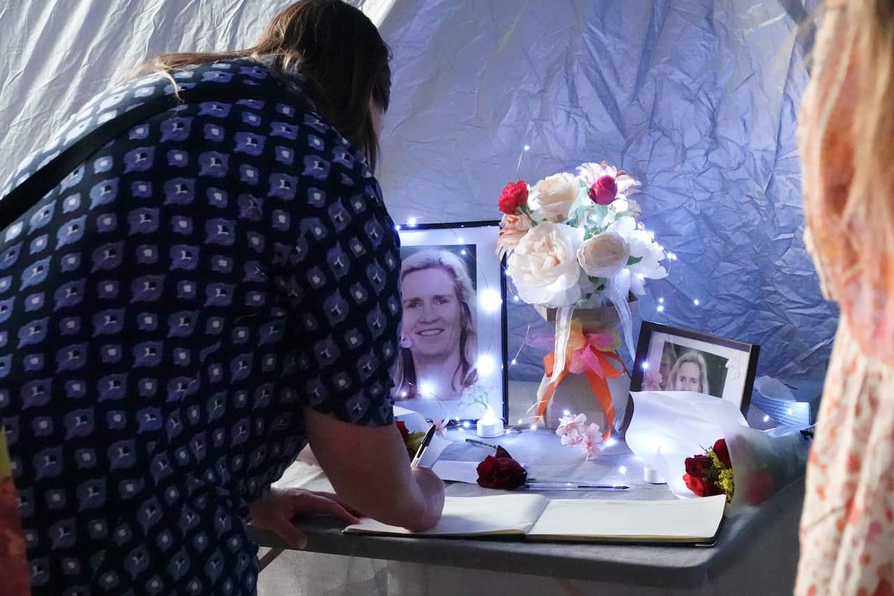 A woman signs a book surrounded by candles and photographs