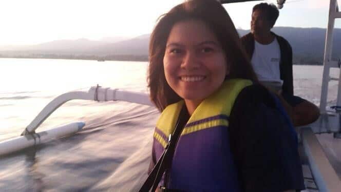 Putu Natih on a boat at sunset with long dark hair and wearing a life jacket. Another boat passenger sits behind her watching the sunset. 