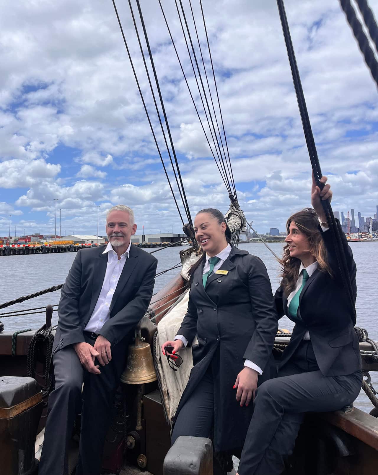 Three people in suits smiling on a ship.