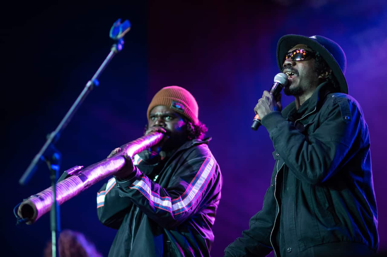 two yolngu men on stage bathed in purple light, one playing yidaki and the other singing into a microphone