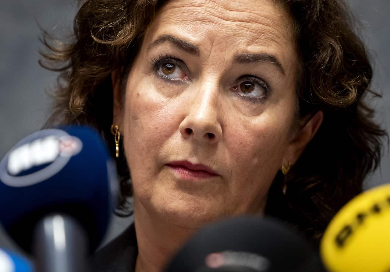 A woman staring ahead while media microphones are in front of her.