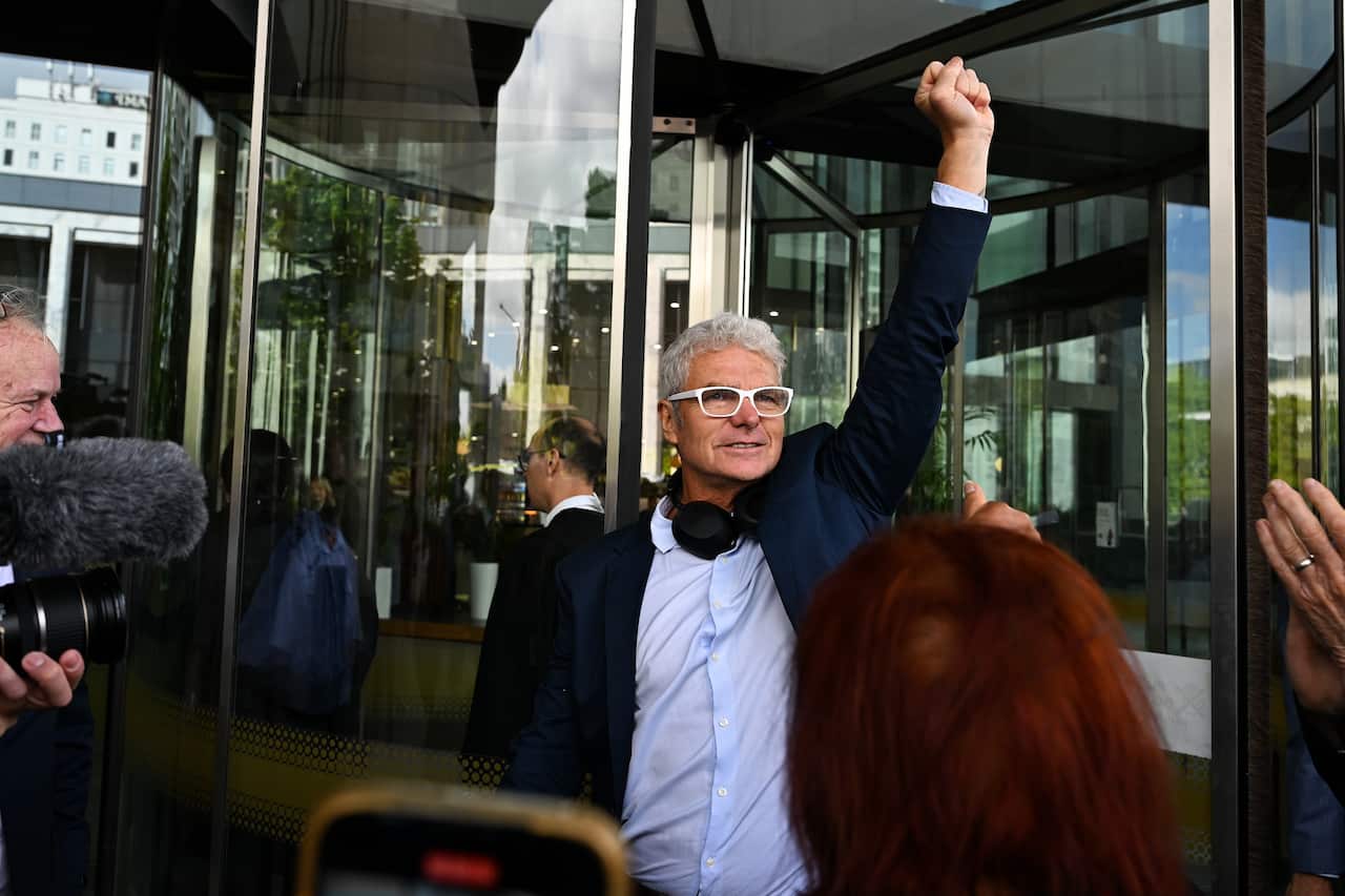 A man raises his fist in the air in front of a building's glass doors.
