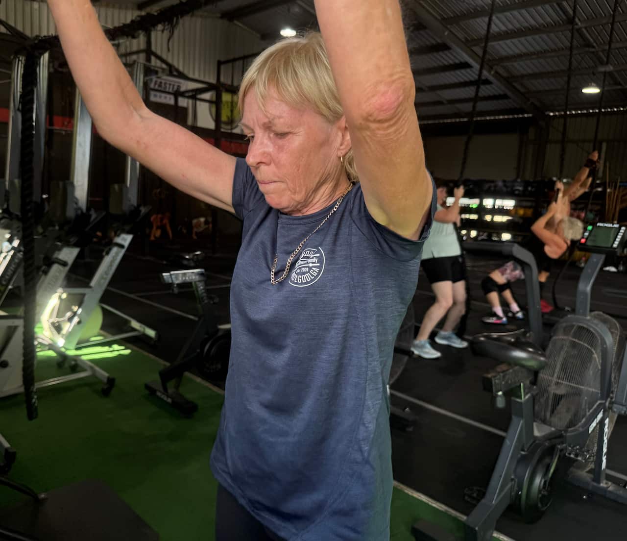 A woman in a blue t-shirt stretching her arms above her head.