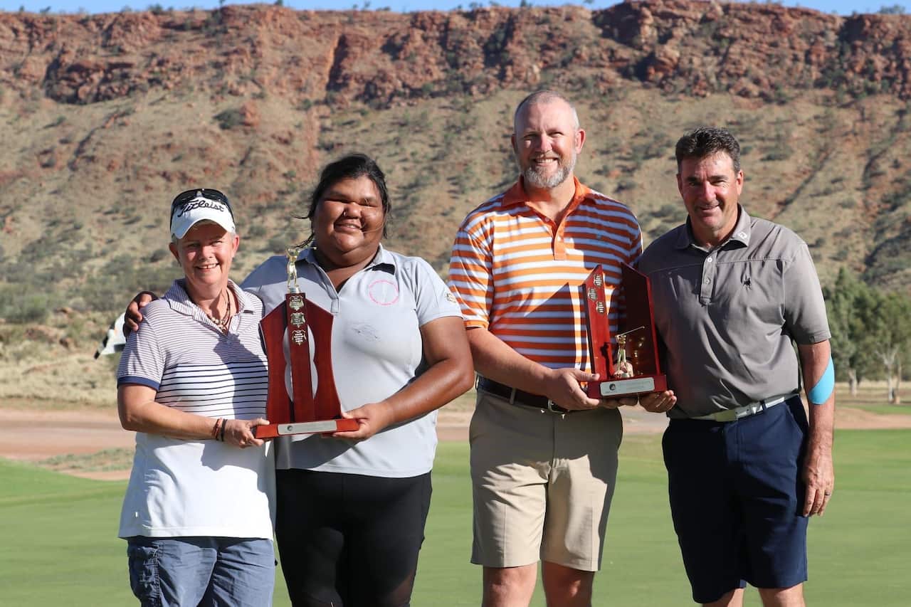 Two men and two women standing outside. Each pair is holding a trophy.