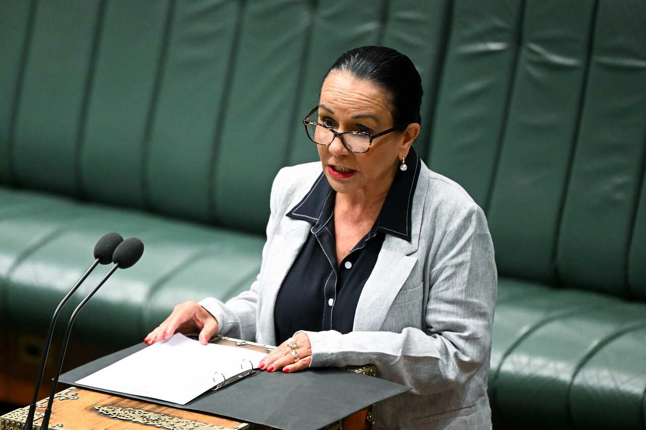 A woman standing and speaking in front of microphones.