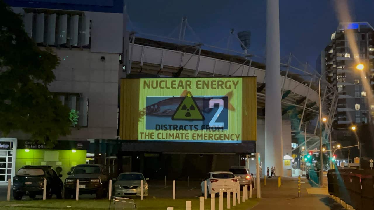An image of a red herring with the text 'Nuclear Energy distracts from the climate emergency' is projected onto a sports stadium