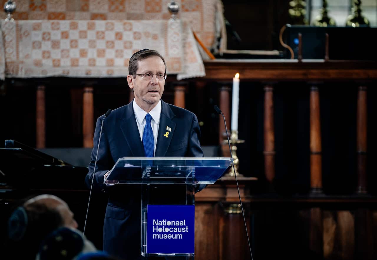 A man wearing a suit and glasses speaking at a podium 