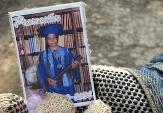 A photo of a young girl in a blue graduation cap and gown, held by a gloved hand.