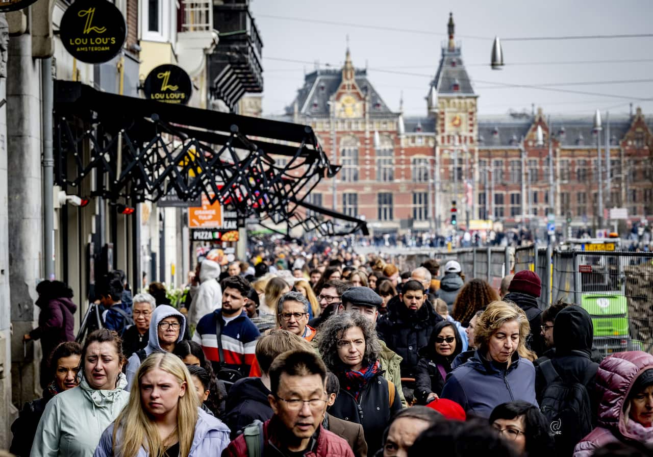 Crowds of people walk down a street in front of a historic building.