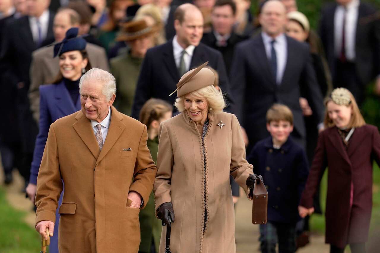 A man and woman in brown coat walking down a road, with a large group of people behind them