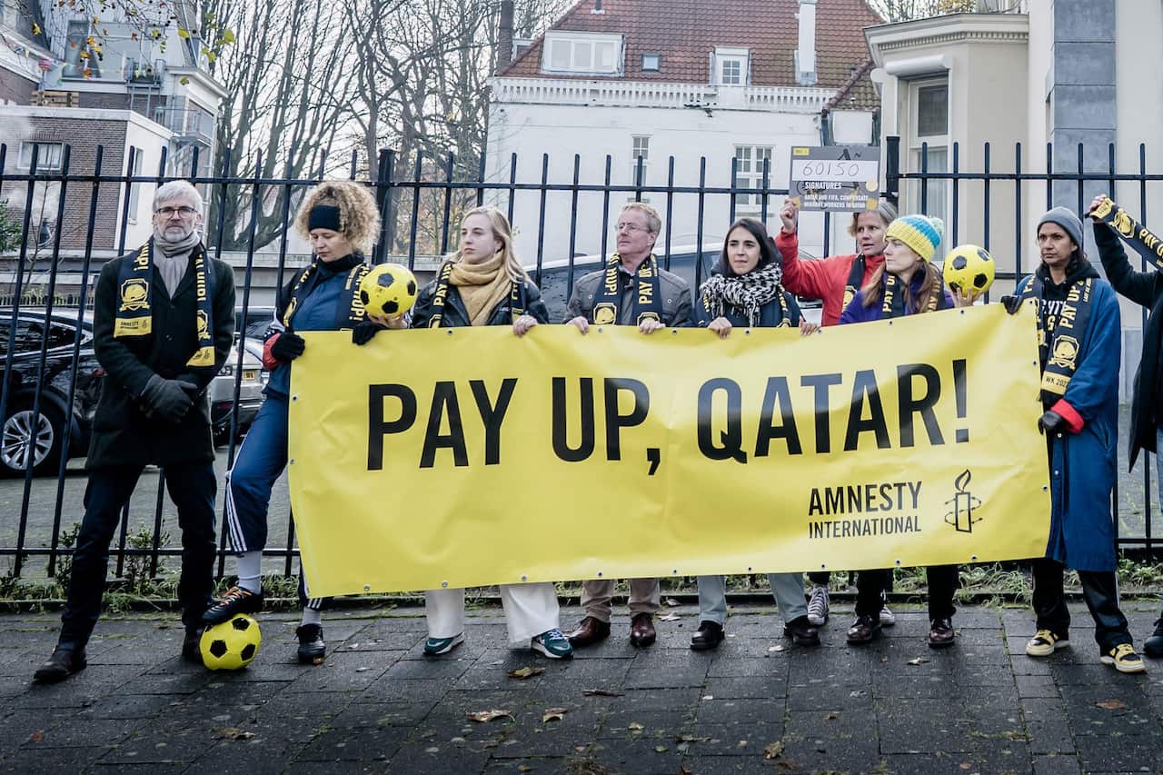 A group of people are standing in line and holding a yellow banner, 'Pay up Qatar'.