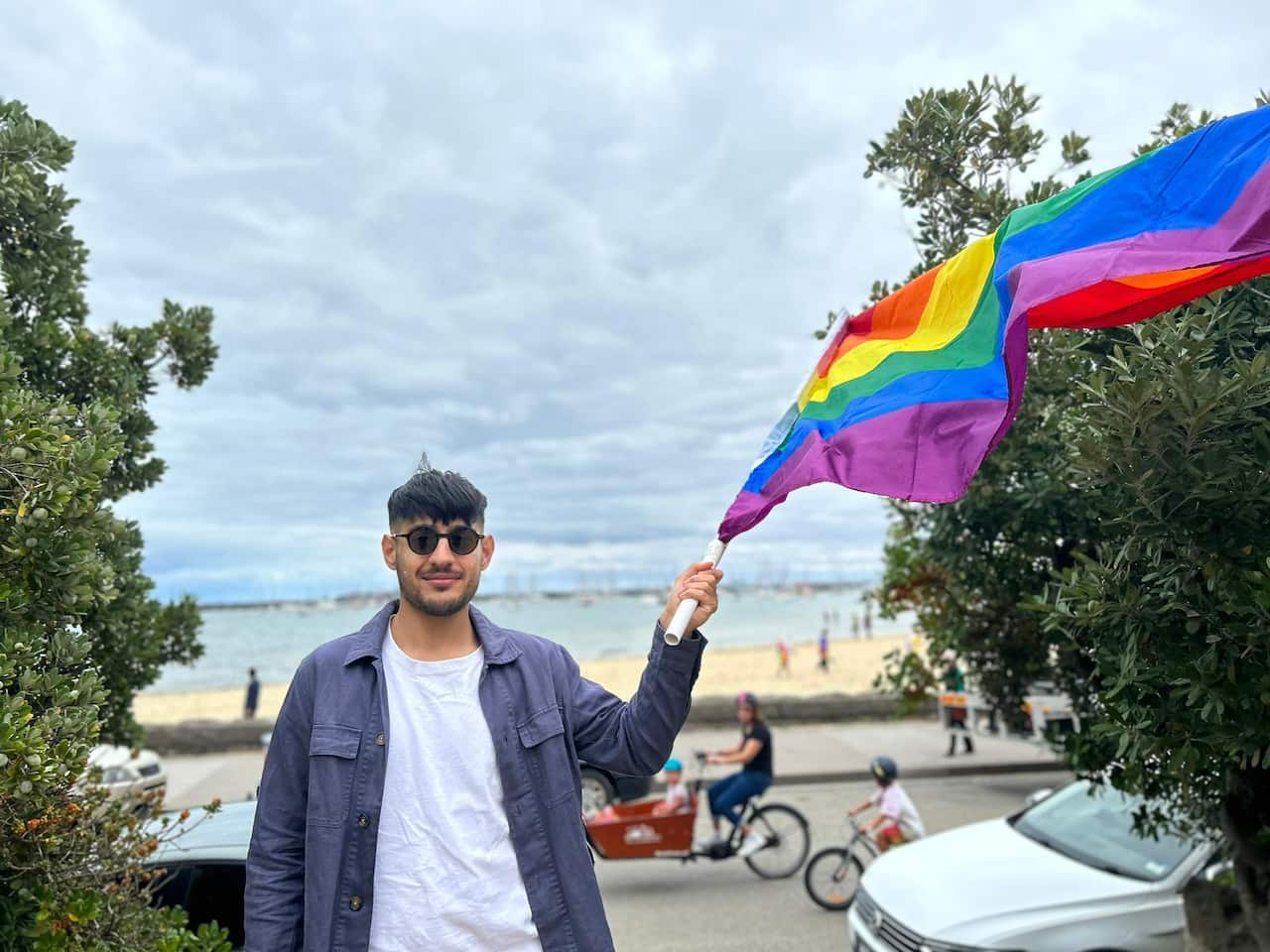 Man wearing sunglasses waves a pride flag. 